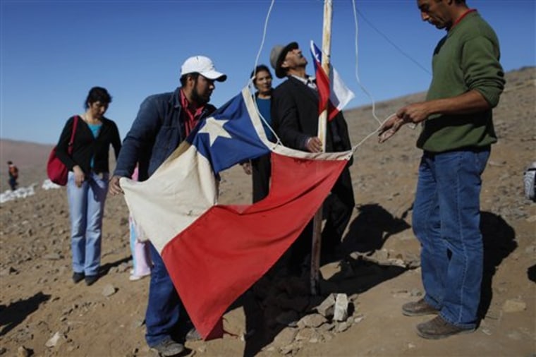 Relatives of miners Renan and Florencio Avalo raise a tattered Chilean flag on a hill overlooking the camp where families wait outside the collapsed San Jose mine in Copiapo, Chile, on Saturday. This flag became a symbol of resilience in Chile when an earthquake survivor was photographed pulling it from the wreckage of the Feb. 27 earthquake.